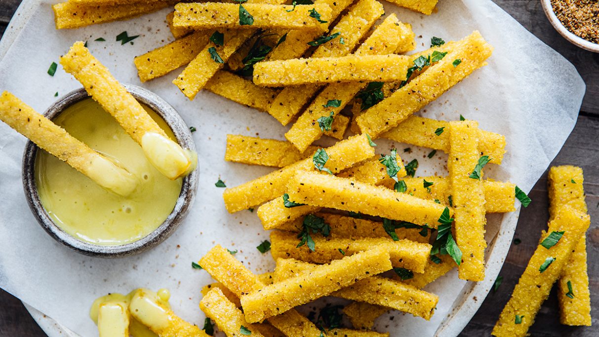 Maisgrieße Sticks aus Polenta sind auf einem Teller angeordnet mit einen Dipp in einer kleinen Schale.